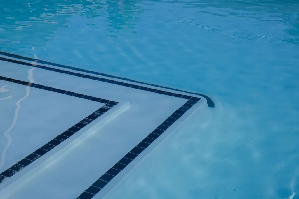 Small robotic pool cleaner resting near pool steps underwater