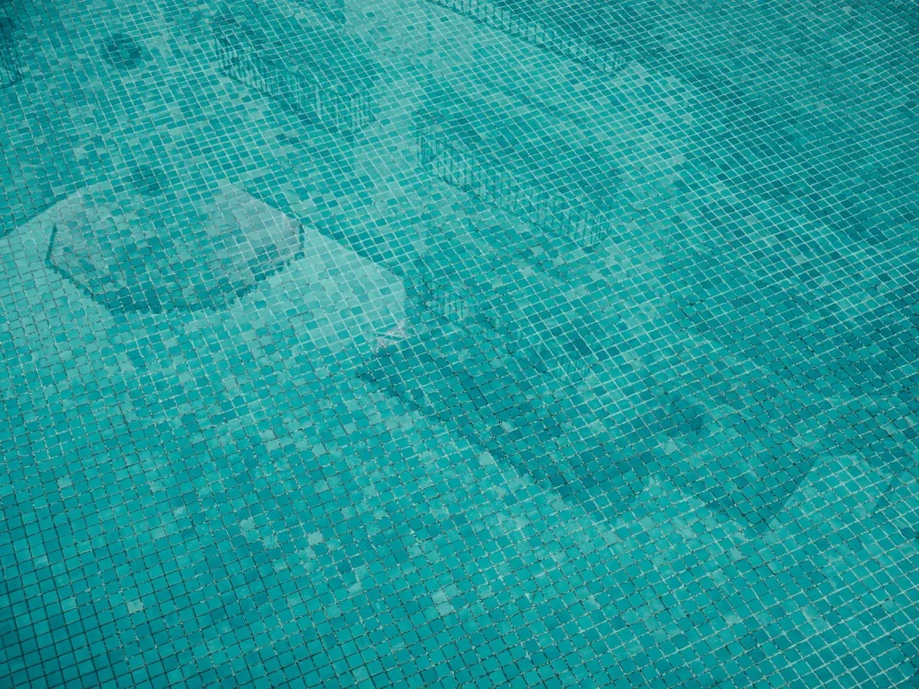 Robotic pool cleaner moving across blue tiles on a sunlit pool floor